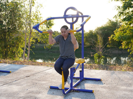 Asian adult woman exercising with outdoor fitness equipment in a park.の写真素材
