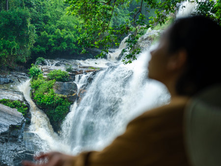 Happy woman enjoying quality time alone on a beautiful waterfall adventure. Female tourist looking at a stunning waterfall.の写真素材
