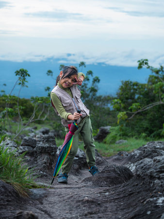 Cute girl smiles and makes a victory gesture looking at the camera while walking on a mountain, family trip in mountains. Mother and children are enjoying nature outdoors.の写真素材