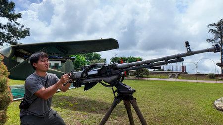 Asian man visits and holds old cannon, weapons used in past battles at Thailand Weapons Museum.の写真素材