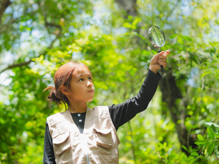 A happy little girl is exploring in the forest and looking for insects with a magnifying glass. Adventure tourism and learning concept.の写真素材