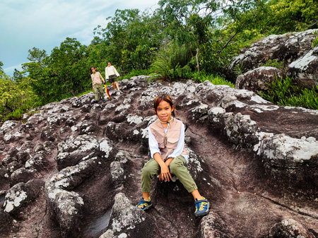 Cute girl smiles and sits down to rest while walking on a mountain, family trip in mountains. Mother and children are enjoying nature outdoors.の写真素材