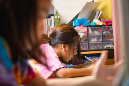 Two elementary school girls are studying at their desks at home. Two cute schoolgirls are diligently doing their homework.の写真素材