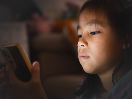 Asian girl using smartphone at night with glowing screen, concept of screen addiction and harmful blue light in childrenの写真素材