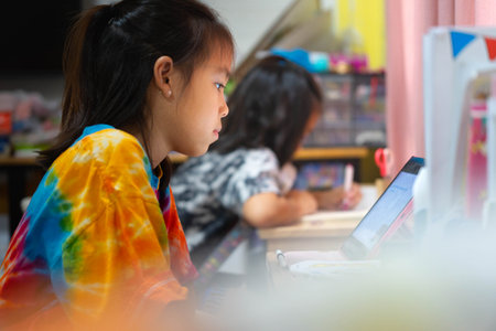 Two Asian schoolgirls studying at home, distance learning and education concept, doing homework together at desk.の写真素材