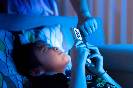 Parent taking smartphone from child at night in bed, concept of screen time limits, digital detox,...