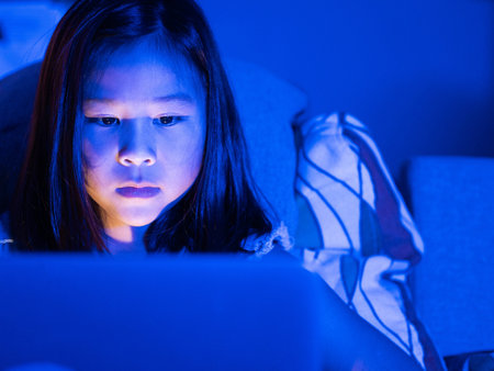 Asian girl sitting on the couch watching laptop at night. Parental control, screen addiction, and bedtime behavior.の写真素材