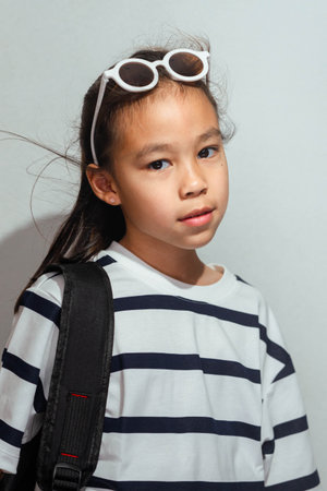 An Asian girl student with a backpack and sunglasses on her head, wearing a striped shirt and looking at the camera.の写真素材