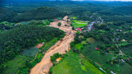 Drone aerial view of muddy floodwaters cutting through farmland and reaching a rural village,...