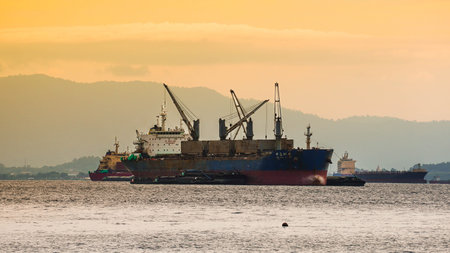 Large cargo ship sailing offshore under dramatic sunset sky, representing global trade and maritime transportation.の写真素材