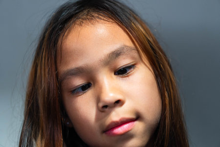 A close-up portrait of a young Asian girl looking downward with curiosity and calmness. Captures authentic emotion and natural beauty, suitable for education, emotion, mindfulness, and childhood development concepts in advertising or editorial use.の写真素材