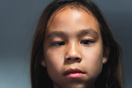 A close-up portrait of a young Asian girl with a serious expression, gazing directly into the...