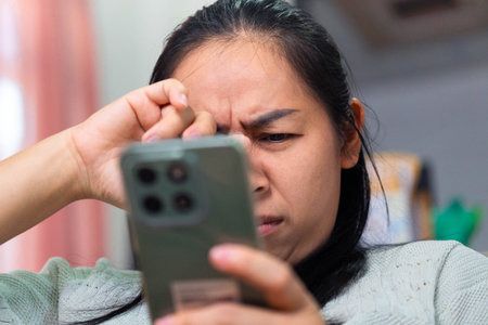 Close-up of an Asian woman suffering from eye strain while looking at a smartphone. The image...