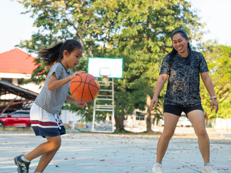 Mother and daughter played basketball together on an outdoor court during sunset.の写真素材