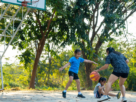 Happy Asian family playing basketball together on outdoor court at the park during golden hour.の写真素材