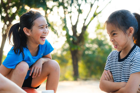 Two happy Asian sisters laughing and making funny faces while playing outdoors.の写真素材