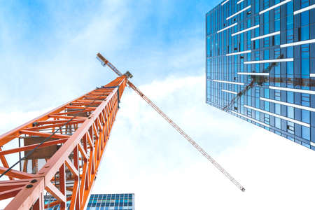 Yellow tower crane. Bottom view of a tall construction crane next to a modern building.の写真素材