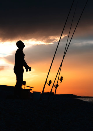 Fisherman cast fishing rods on the seashore at a dramatic sunset. Fisherman silhouette. Night...