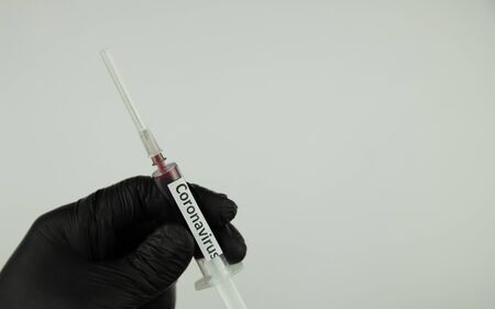 coronavirus spread concept, syringe labeled coronavirus in hand, black glove on a white background