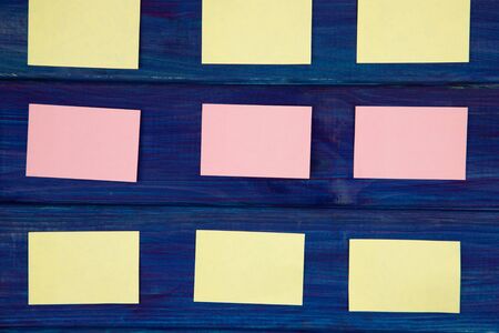 yellow and pink pieces of paper for notes on a blue wooden background - horizontal image top...