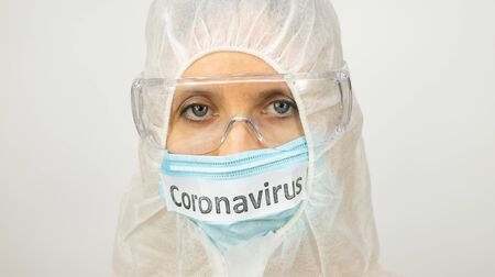 face of a white woman in a medical mask - inscription coronavirus, safety glasses and a suitの写真素材