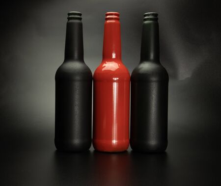 two black and one red bottles stand next to a black background, close-upの写真素材