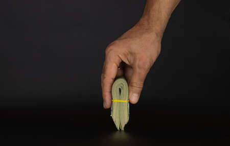 A pack of ten thousand dollars folded in half in a man's hand, black background