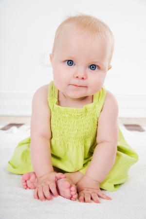 pretty baby girl with big blue eyes sits in  green dress の写真素材
