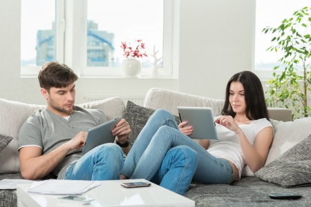 couple sitting on a sofa in the living room, using a tablet computerの写真素材