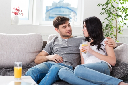 young couple sitting on a couch and drinking orange juiceの写真素材