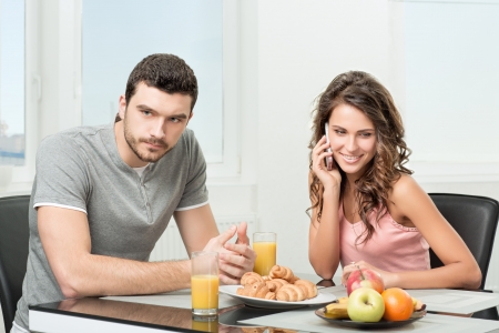young beautiful couple having breakfast, girl talking on the phoneの写真素材