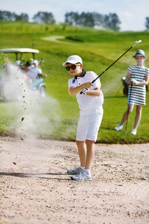 Boy playing golf and hitting from bunkerの写真素材