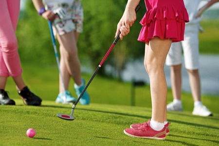 Legs of kids playing golf and hitting by putter on greenの写真素材