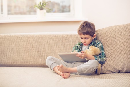 Cute little boy playing with a tablet pc on sofa at homeの写真素材