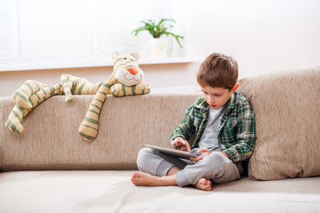 Cute little boy playing with a tablet pc on sofa at homeの写真素材