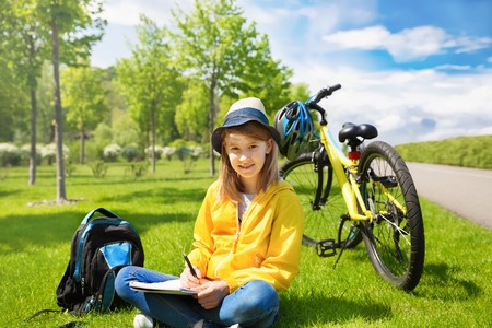 Teenage girl biker sitting on a green grass next to a mountain bike and and drawsの写真素材