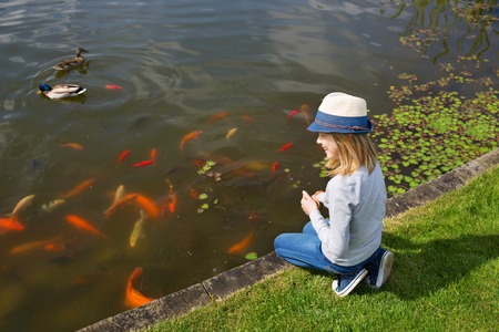 Happy girl teenager feeding fishes in a garden pondの写真素材