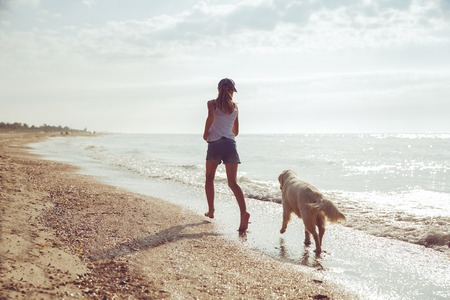Teenage girl running along a beach shore with her golden retriever during the early morning.の写真素材