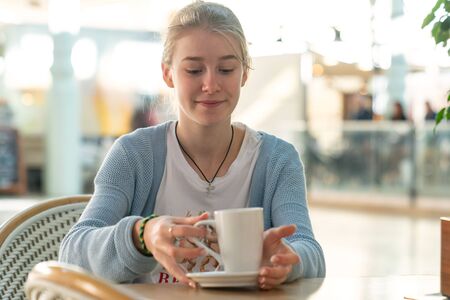 Happy young teenage girl with cup drinking coffee at city street cafe terrace and dreamingの写真素材