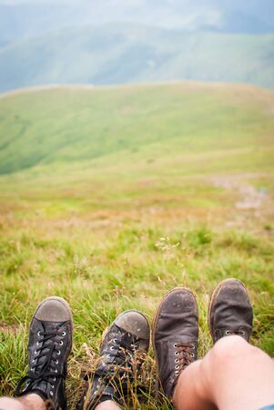 Two pairs of travelers' shoes against green hill in Carpathian mountainsの写真素材