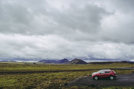 Red and gray offroad cars by a green Icelandic field with purple mountains on the background. Cloudy...