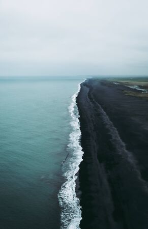 Turquoise water, white foam, and black sand. Magical and calm atmosophere in Vik, Iceland.の写真素材
