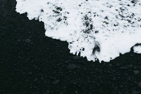 White oceanic water covering blackest sand of Icelandic beach.の写真素材