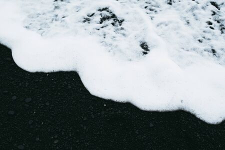 White ocean water and black sand beach in Icelandの写真素材