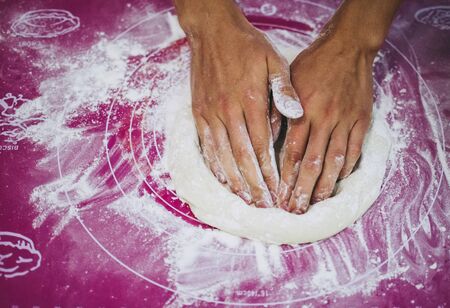Pizzaiolo kneading pizza dough with his hands, purple background. Homemade pizza preparation process