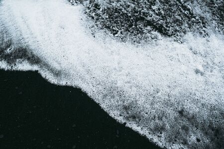 White ocean water and black sand beach in Icelandの写真素材