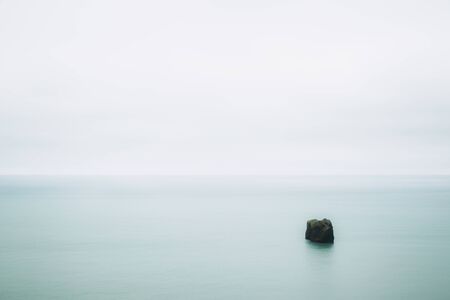Smooth turquoise water of the Atlantic ocean and a small piece of rock in it. Calmness and minimalism. South Icelandの写真素材