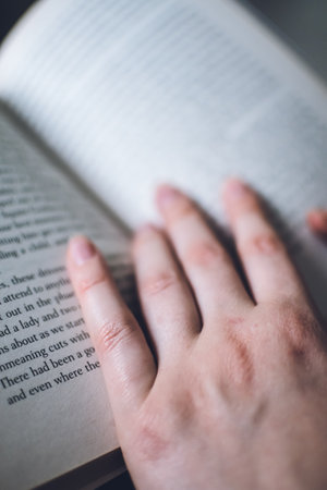 A girl reading a book and following along the lines with her pale tender fingersの写真素材