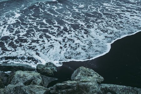 Cold waters of Atlantic Ocean on black sand beach in Iceland. View from gray rocks.