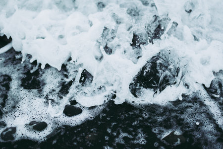 Transparent piece of glacier in the white Icelandic waters of Atlantic ocean on the black beach